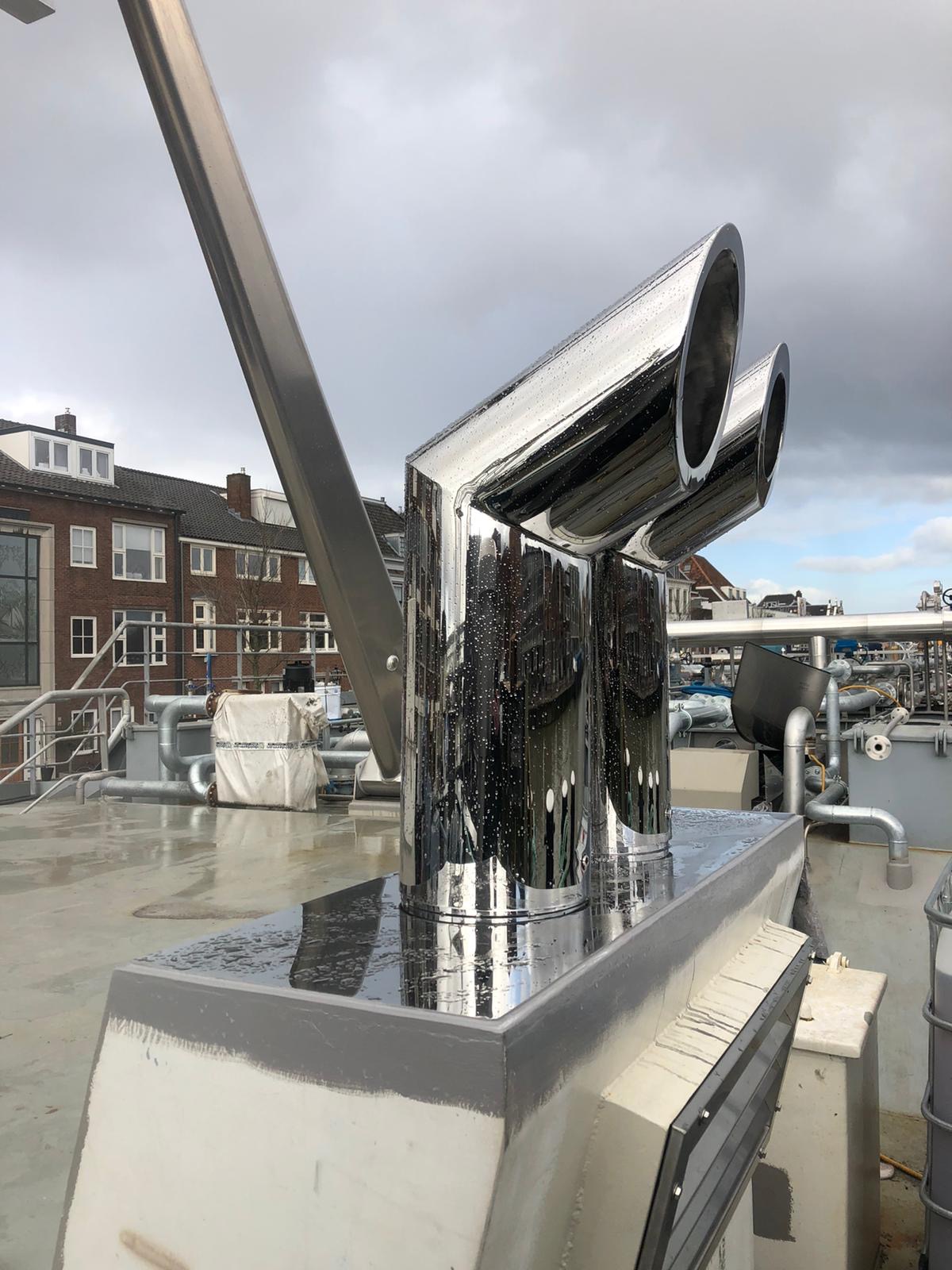 Błyszcząca, potrójna rura wentylacyjna ze stali nierdzewnej na dachu budynku, widoczne krople wody po deszczu.