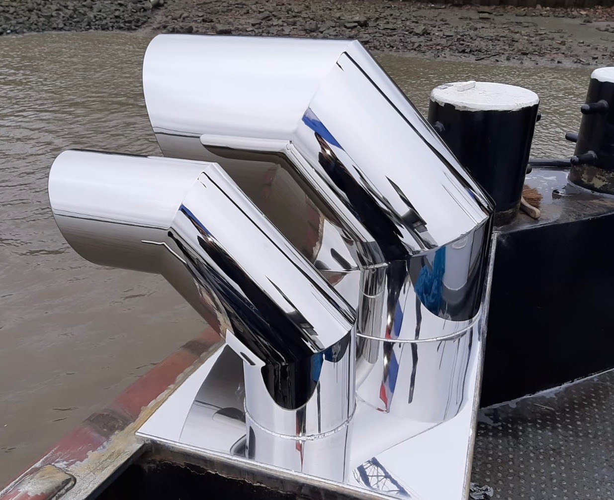 Błyszczące, nierdzewne rury gięte pod kątem na konstrukcji w Kębłowie, odbijające otoczenie, prawdopodobnie element większej instalacji.