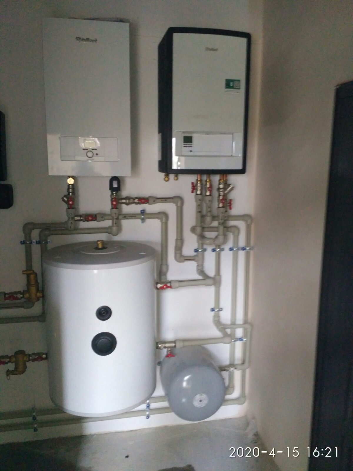 Dwa kotły grzewcze marki Vaillant, biały i czarny, zamontowane na ścianie, z widoczną instalacją hydrauliczną, zbiornikiem na wodę i naczyniem przeponowym. Widoczne zawory i rury z tworzywa...