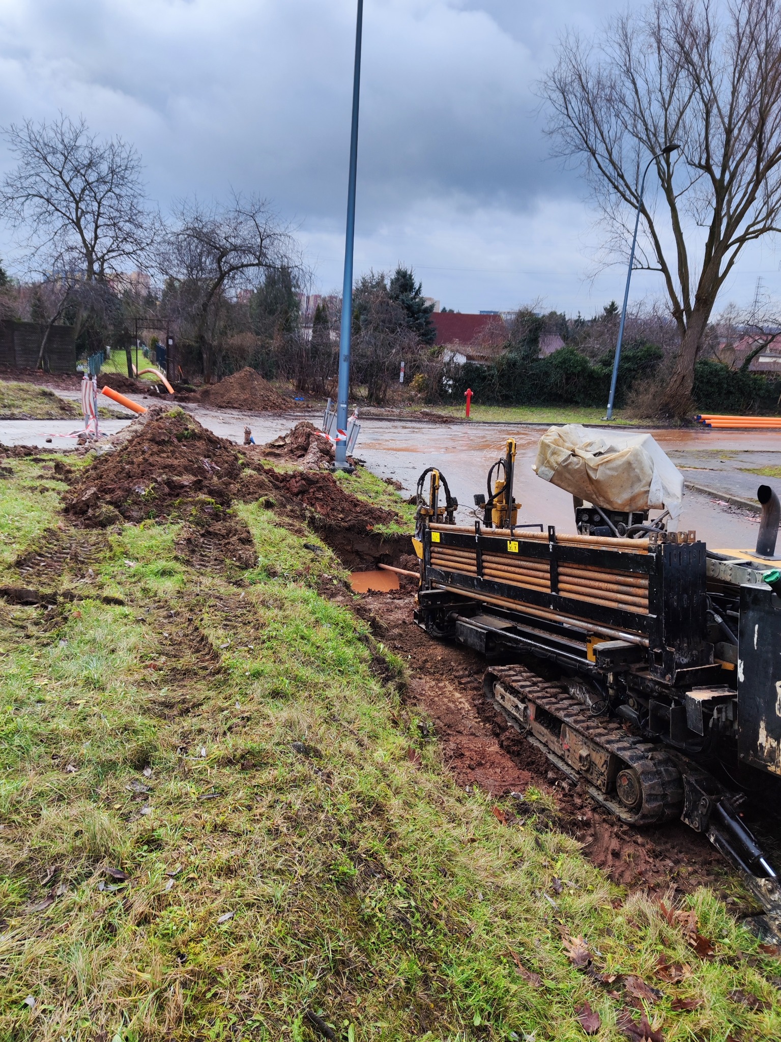 Maszyna do przewiertów horyzontalnych na placu budowy, widoczne rury i wykop. Pochmurne niebo w tle. Prace ziemne w toku.