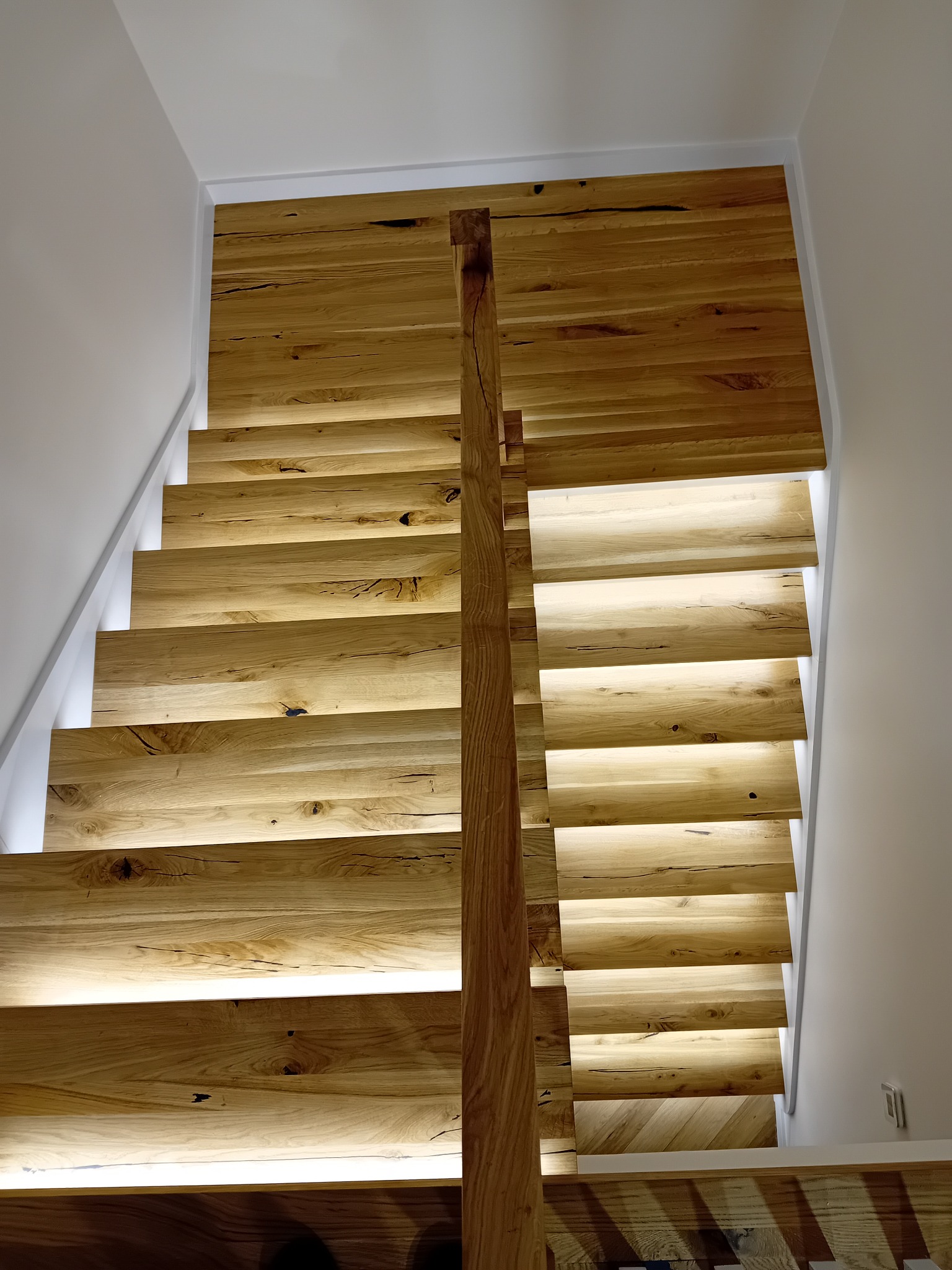 Drewniane schody z podświetleniem LED, widok z góry. Naturalne drewno z widocznymi słojami i sękami. Minimalistyczny design w jasnej kolorystyce.