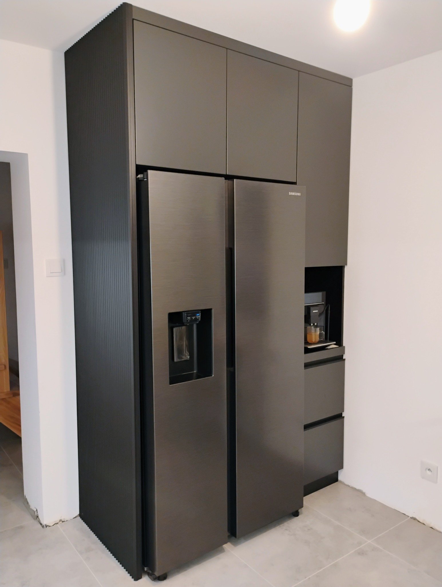 Nowoczesna kuchnia na wymiar: zabudowa w odcieniach szarości z lodówką side-by-side Samsung i wbudowanym ekspresem do kawy. Minimalistyczny design.