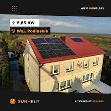 Dom jednorodzinny z czerwonym dachem, na którym zamontowano czarne panele słoneczne. Widoczne oznaczenie lokalizacji 'Woj. Podlaskie' oraz informacja o mocy instalacji 5,85 kW. W tle krajobraz...