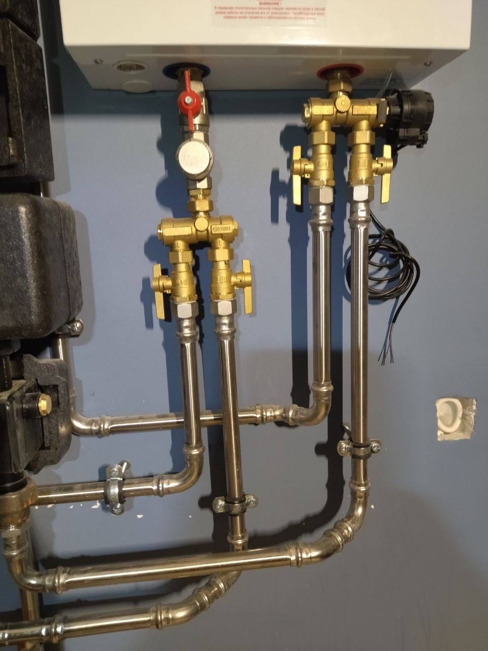 Szczegółowe ujęcie instalacji hydraulicznej z zaworami i rurami w kolorze złotym i srebrnym, zamontowanej na szarej ścianie w Warszawie, widoczne elementy kotła.