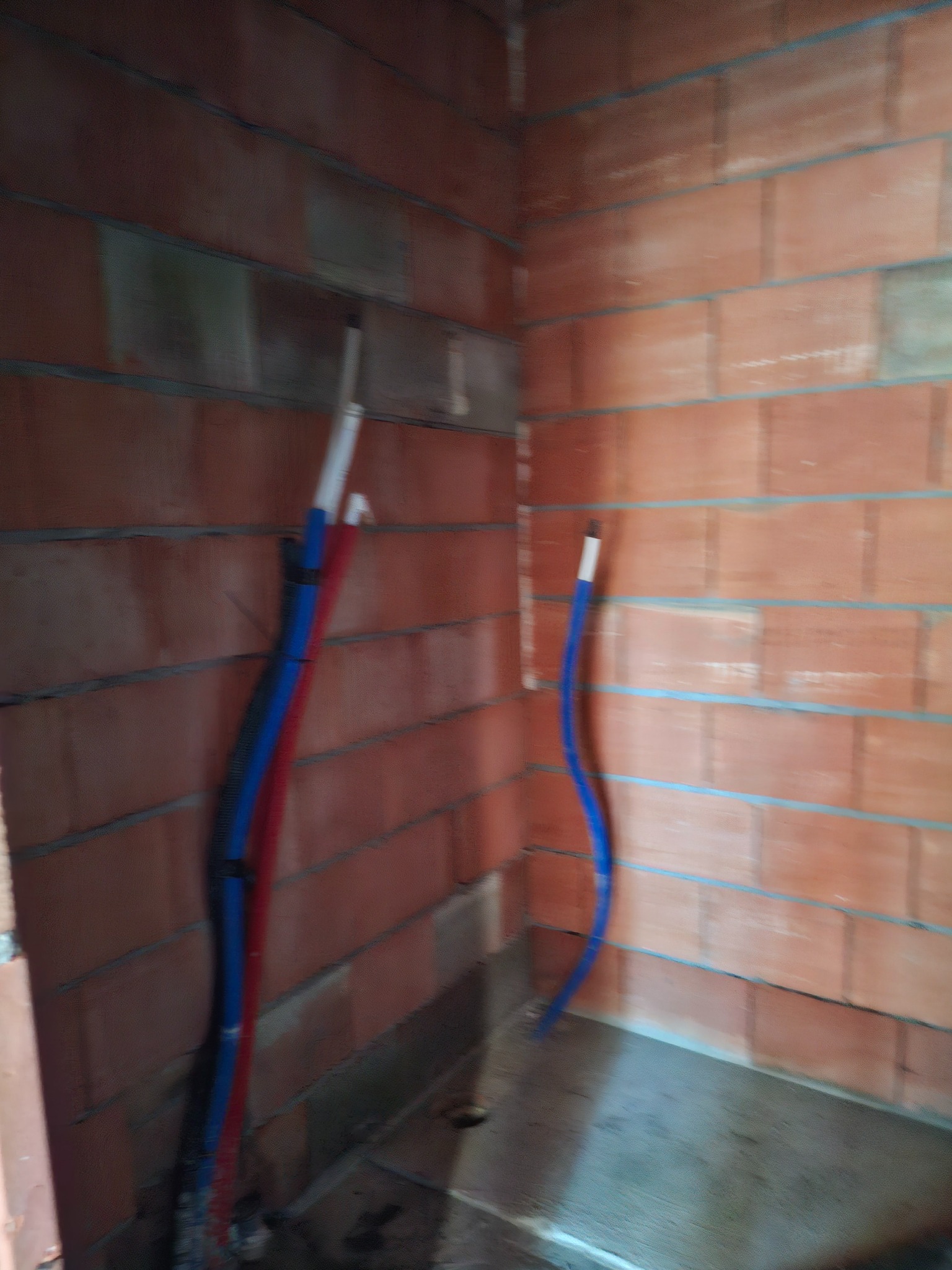 Wewnętrzna ściana z czerwonej cegły z widocznymi rurami instalacji wodnej w kolorze niebieskim i czerwonym.