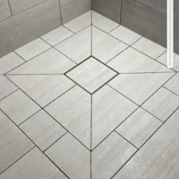 Szare płytki ceramiczne ułożone w geometryczny wzór na podłodze i ścianach kabiny prysznicowej z odpływem liniowym w kształcie kwadratu.
