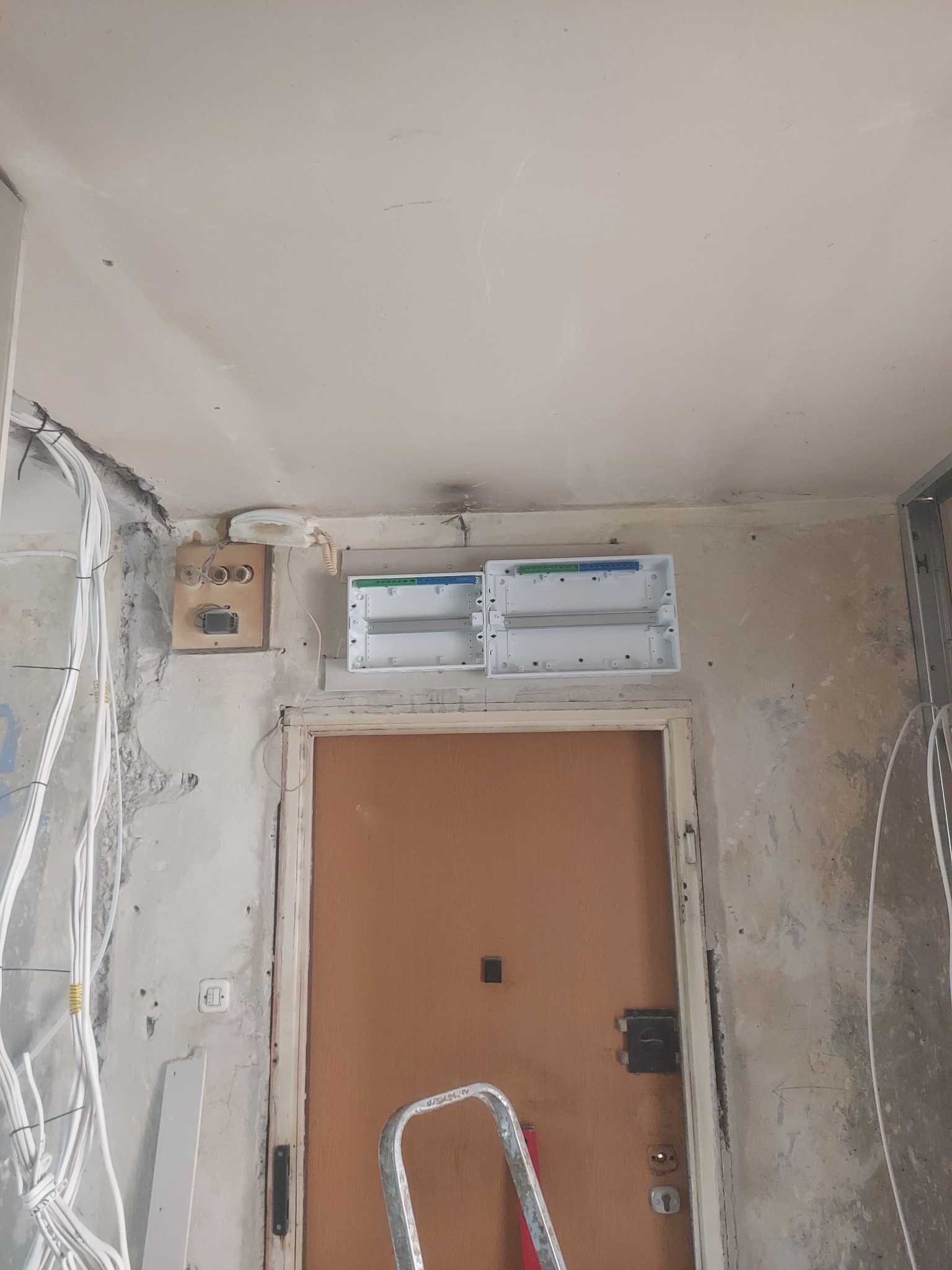 Przygotowanie do montażu skrzynki elektrycznej nad drzwiami wejściowymi w mieszkaniu we Wrocławiu, widoczne kable i stara instalacja telefoniczna.