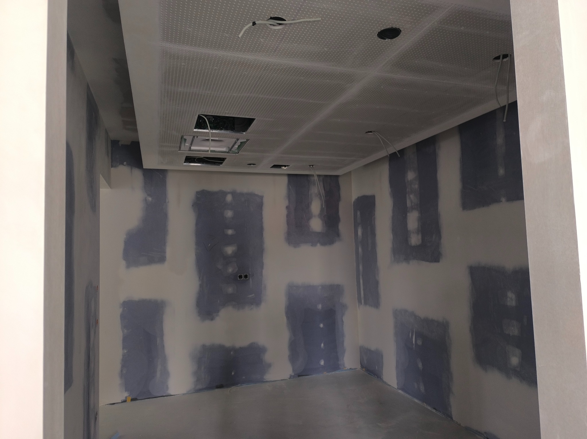 Wnętrze pokoju w trakcie remontu, ściany z widocznymi łatami po szpachlowaniu, sufit podwieszany z płyt kartonowo-gipsowych z otworami na oświetlenie i instalacje.