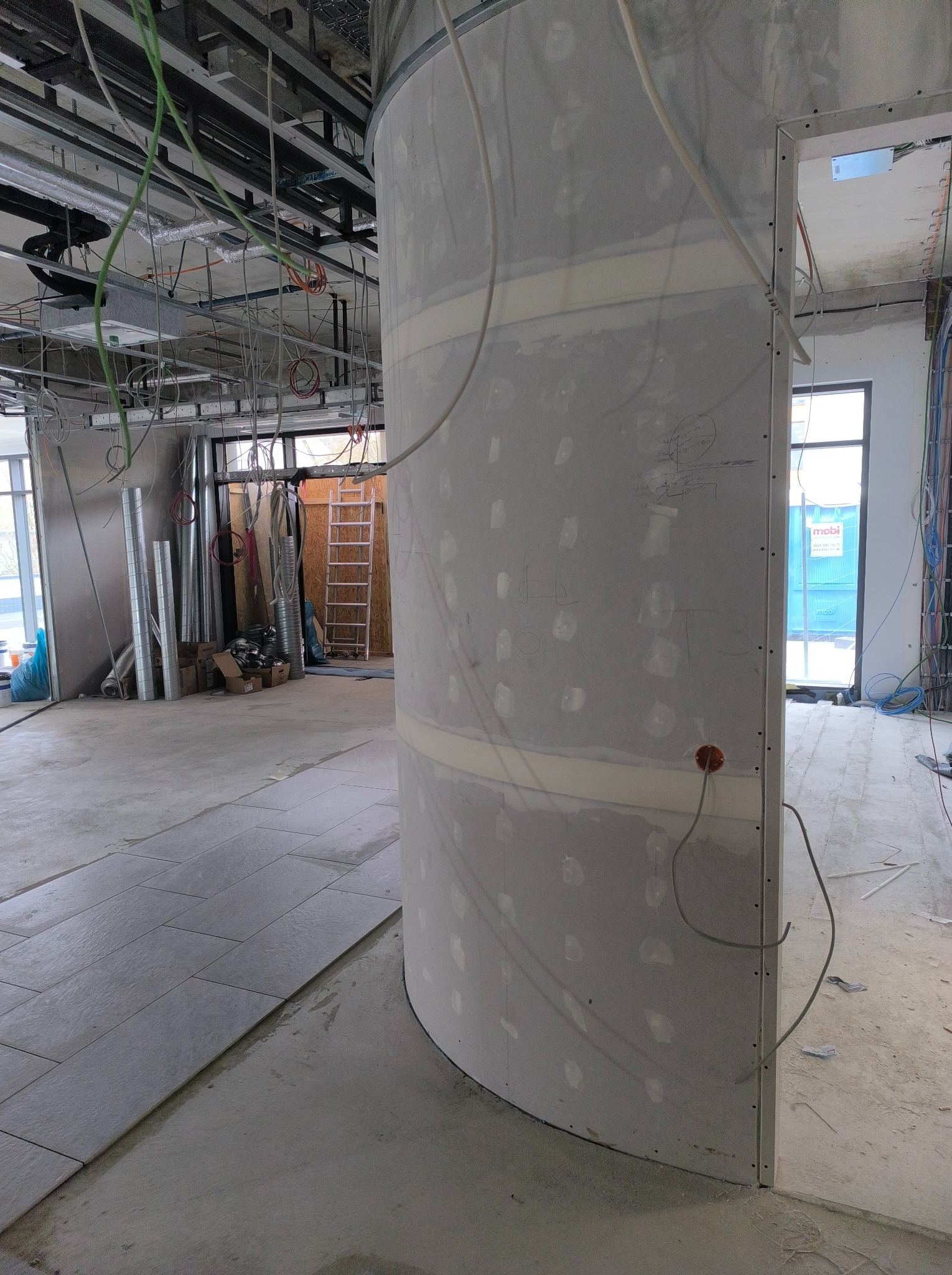 Wnętrze w trakcie wykańczania z widoczną zaokrągloną ścianą z płyt gipsowo-kartonowych, częściowo zaszpachlowaną, odsłonięta instalacja elektryczna na suficie, ułożona podłoga z płytek, widoczne...