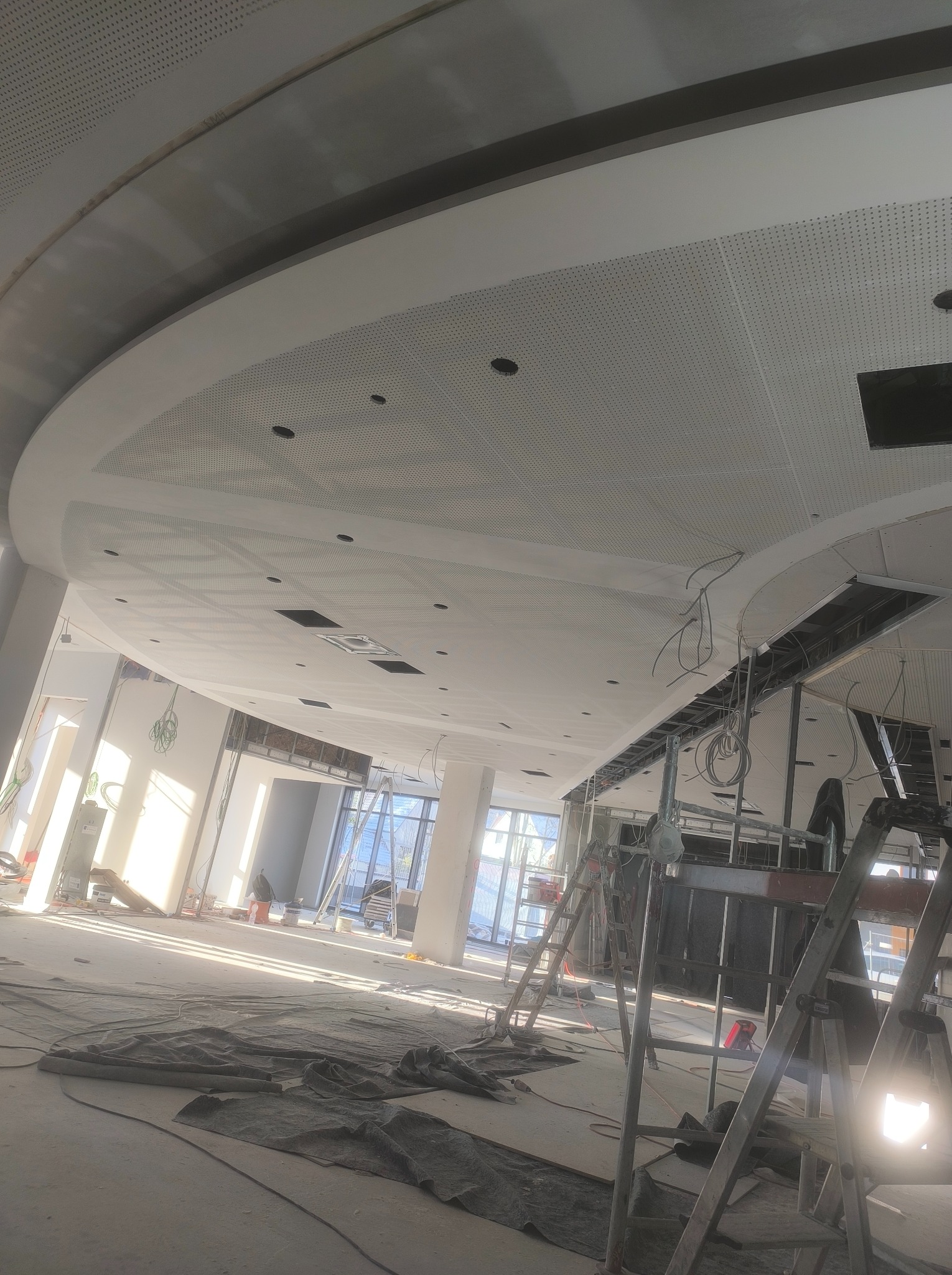 Montaż perforowanego sufitu podwieszanego z płyt karton gips w dużej hali, widoczne drabiny i kable