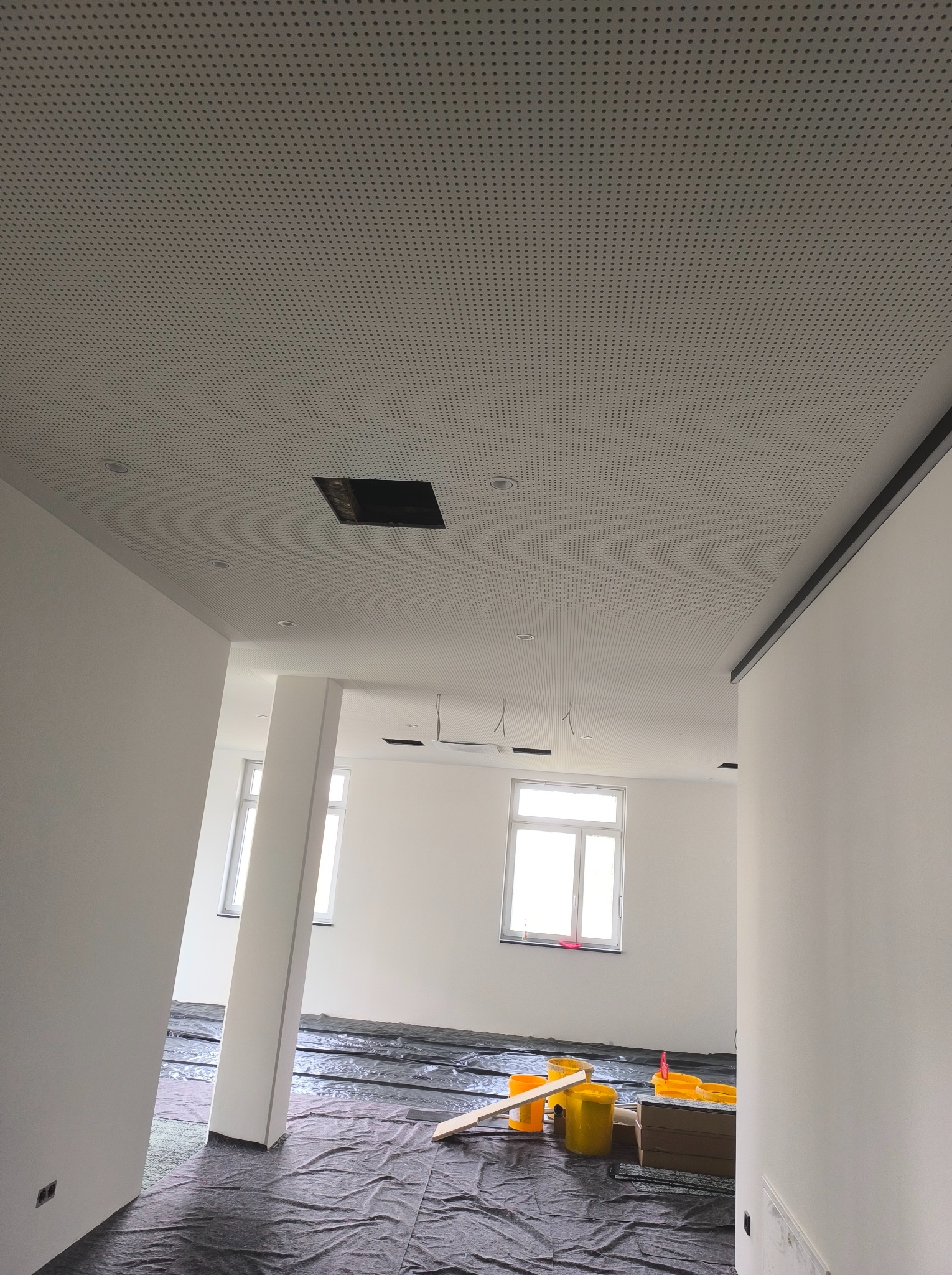 Montaż sufitu podwieszanego z perforowanej płyty w lokalu w Warszawie, widoczne żółte wiadra i folia ochronna na podłodze.