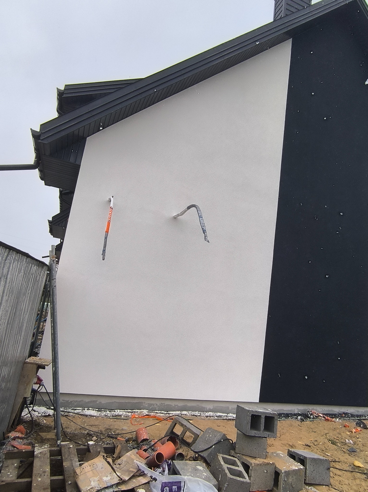 Biało-czarna elewacja domu po renowacji, widoczne elementy instalacji i gruz budowlany. Kontrastowe barwy elewacji, nowoczesny design.