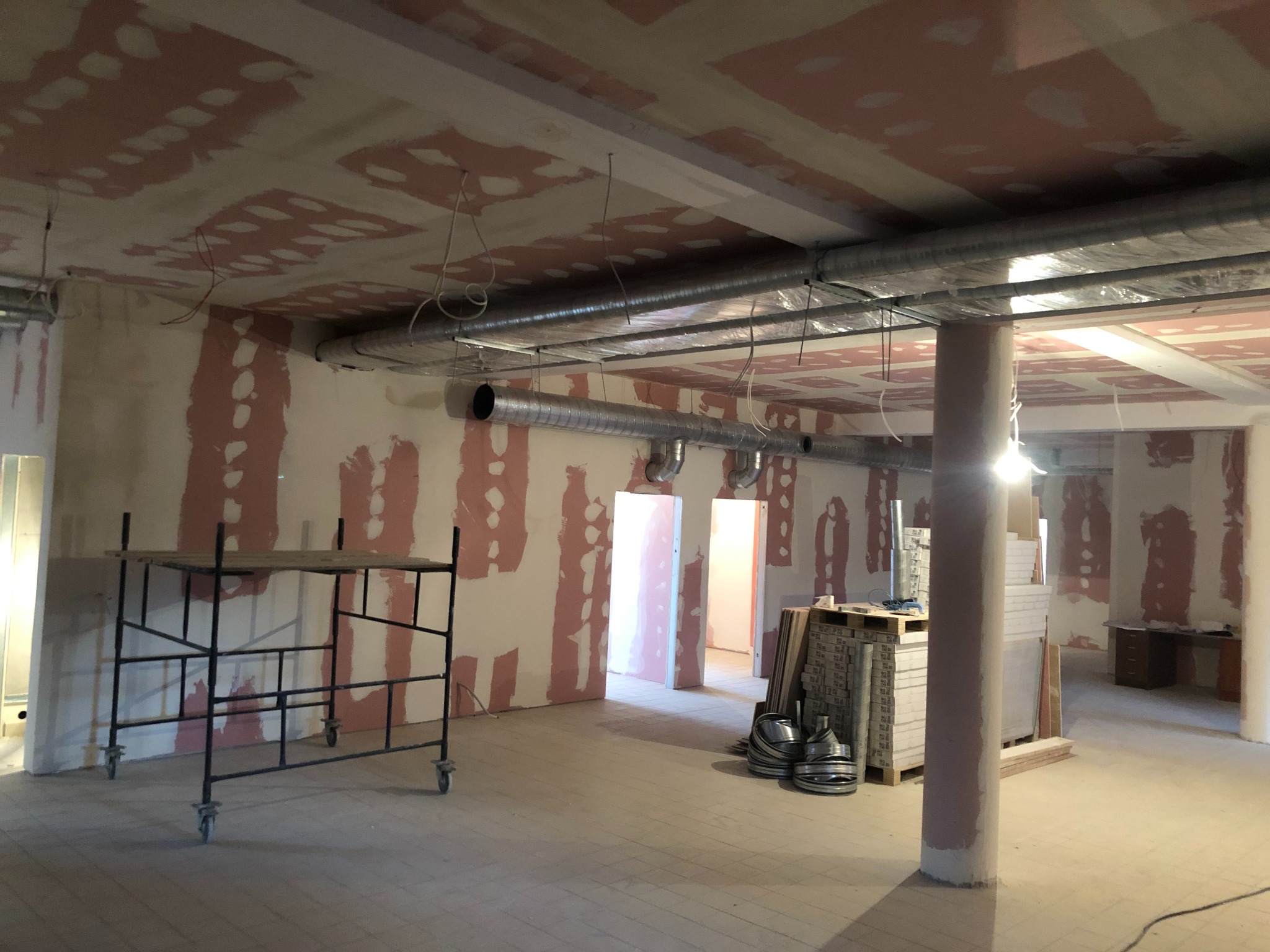 Wnętrze w trakcie remontu: widoczne rusztowanie, materiały budowlane, surowe ściany z nałożoną gładzią, instalacja wentylacyjna pod sufitem, oraz częściowo wykończona podłoga.