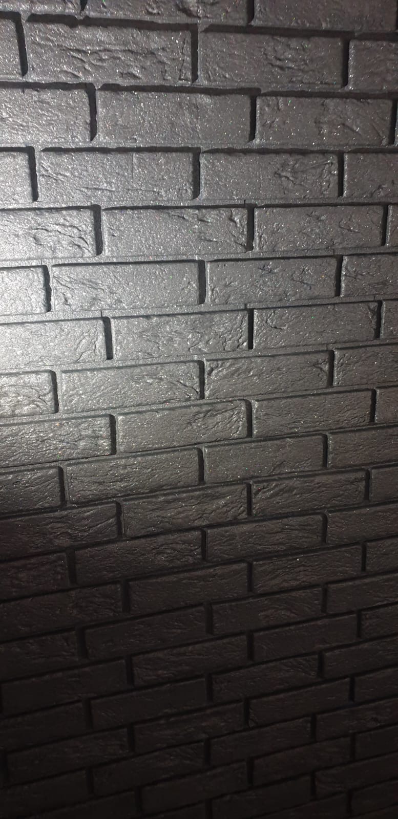 Ściana wyłożona czarną, błyszczącą cegłą dekoracyjną o wyraźnej fakturze, ułożoną w regularny wzór.