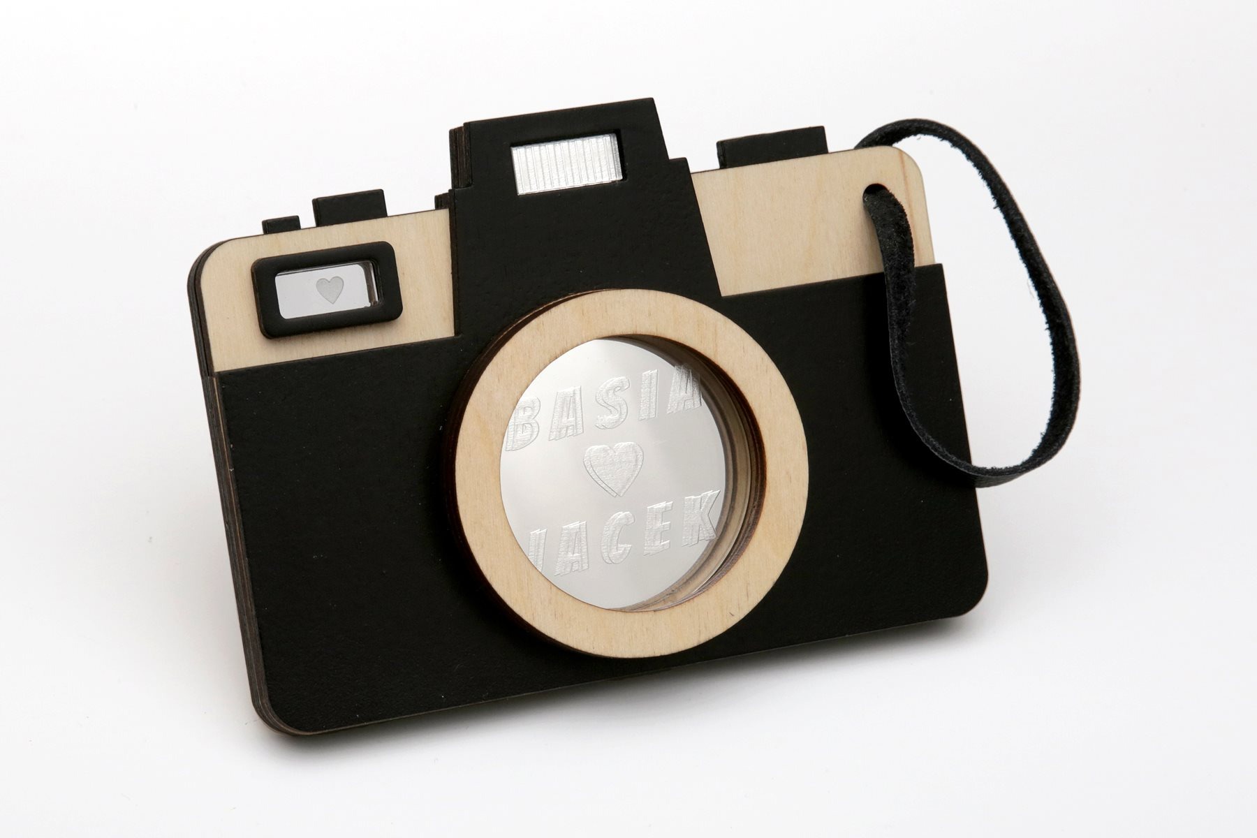 Drewniana zawieszka w kształcie aparatu z lusterkiem i grawerem imion Basia i Jacek, na białym tle.