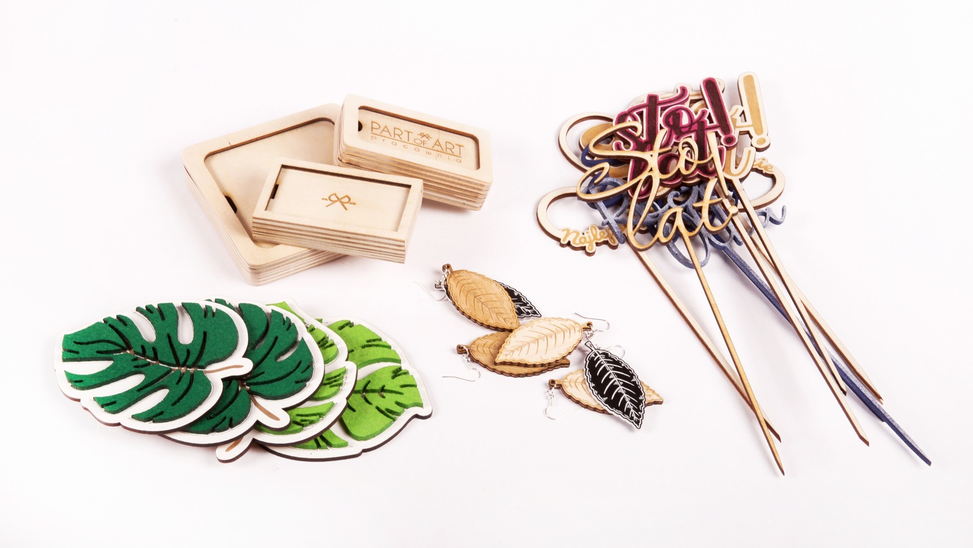 Ręcznie robione, drewniane i filcowe ozdoby: pudełka z logo, kolczyki w kształcie liści, dekoracje na piku z napisami na białym tle.