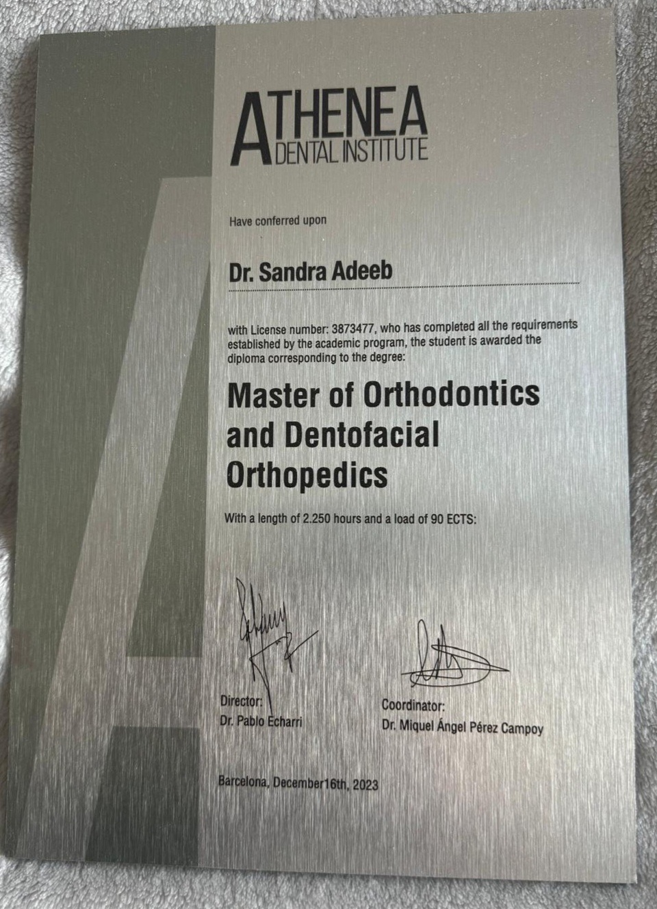 Dyplom ukończenia studiów Master of Orthodontics and Dentofacial Orthopedics dla Dr. Sandry Adeeb, wydany przez Athenea Dental Institute, z podpisami dyrektora i koordynatora, na srebrnym tle.