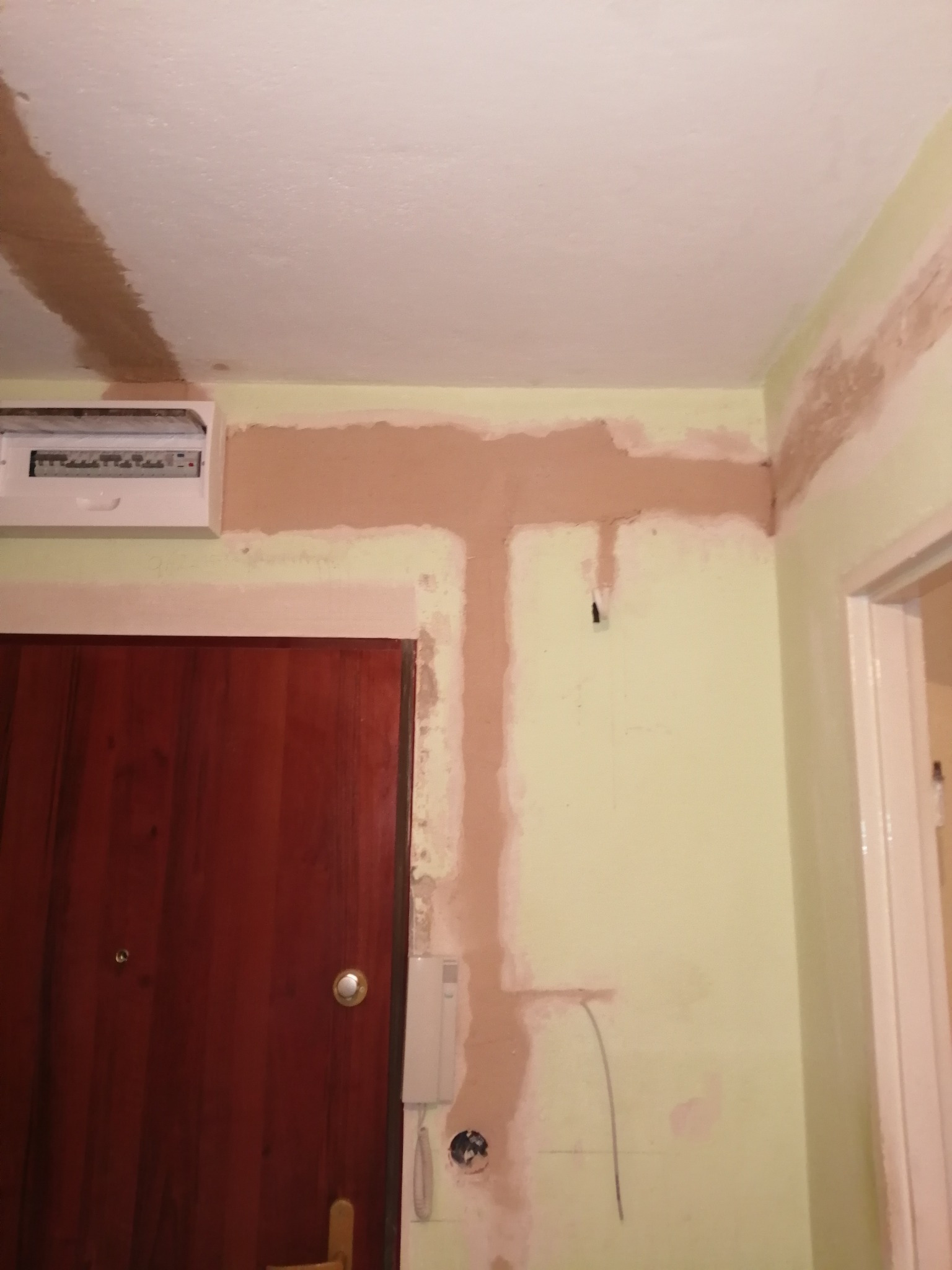 Ściana po bruzdowaniu pod instalację elektryczną, widoczna puszka z bezpiecznikami, kable wystające ze ściany i ślady po gładzi szpachlowej.