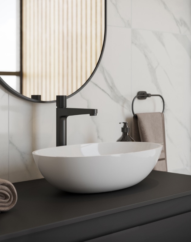 Nowoczesna łazienka: biała, owalna umywalka nablatowa z czarną armaturą na tle marmurowej ściany i okrągłego lustra.