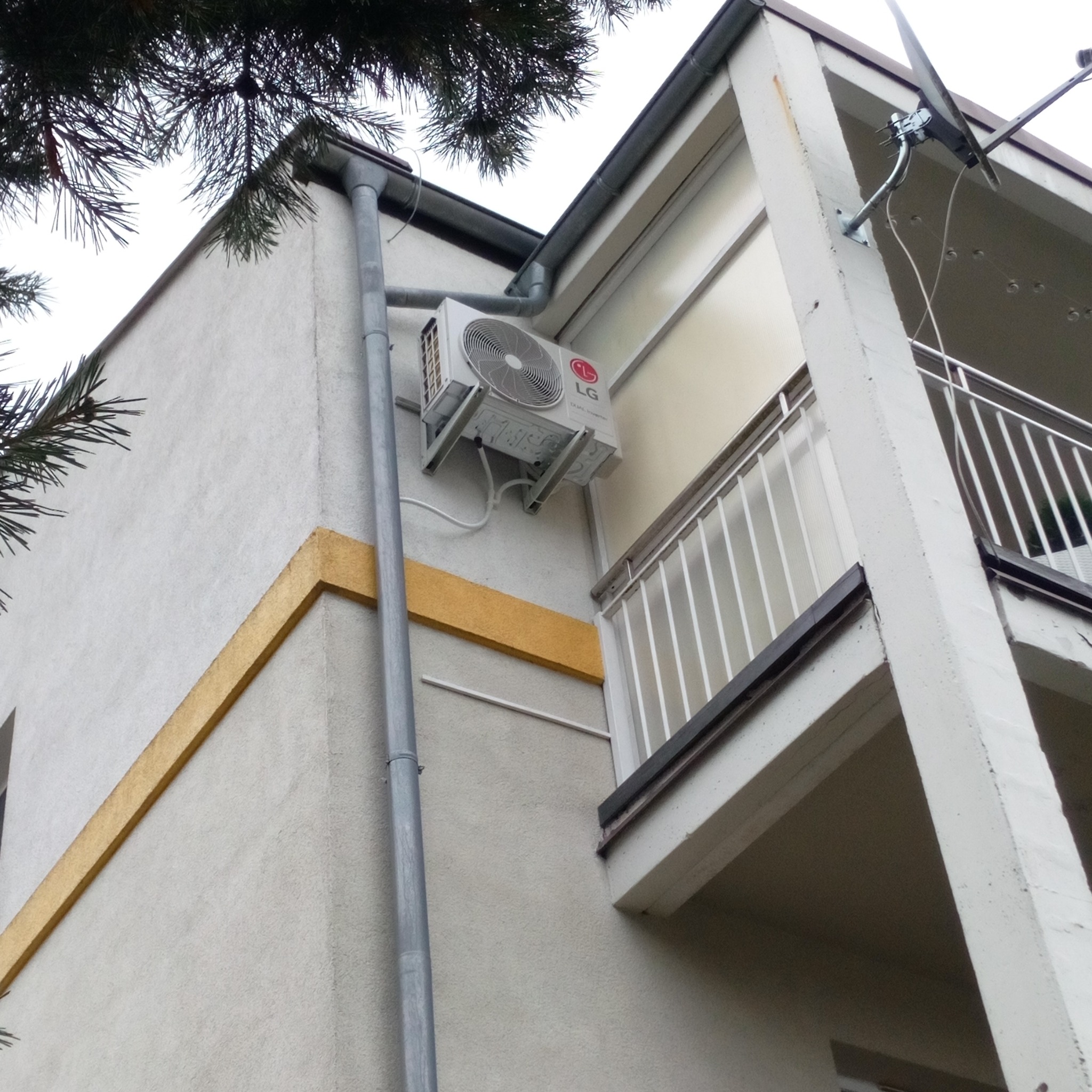 Zewnętrzna jednostka klimatyzacji LG zamontowana na ścianie budynku w Drezdenku, widoczna z boku, z rurą spustową i fragmentem balkonu w tle.