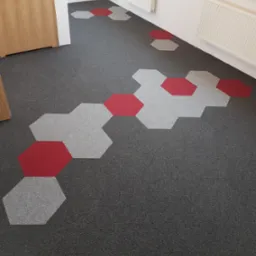 Szara wykładzina dywanowa w biurze z wzorem heksagon&oacute;w w kolorze szarym i czerwonym, widoczny fragment drzwi i grzejnika