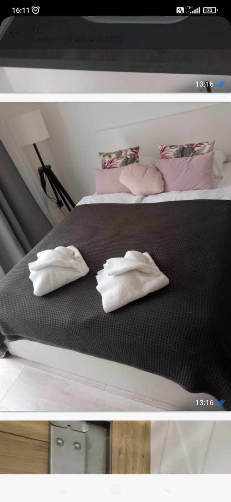 Starannie posłane łóżko w pokoju gościnnym z dekoracyjnymi poduszkami i złożonymi ręcznikami, gotowe na przyjęcie gości. Widoczna lampa i zasłony.