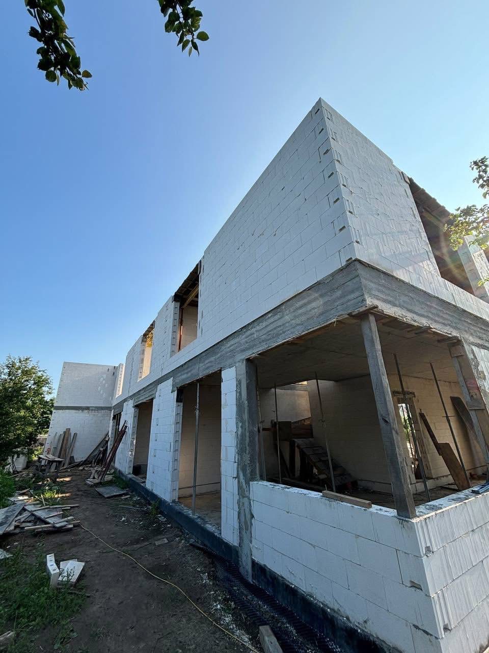 Nieotynkowany, dwukondygnacyjny dom z białego betonu komórkowego w trakcie budowy, z widoczną konstrukcją schodów wewnętrznych i fragmentem nieba.