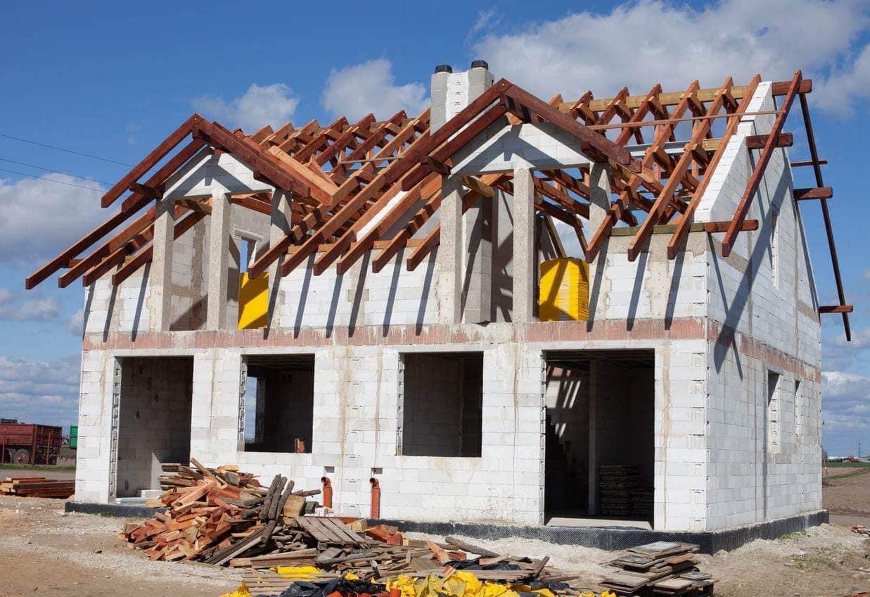 Surowy stan domu z pustaków w Надвірна z widoczną konstrukcją dachu i stertą drewna na placu budowy.