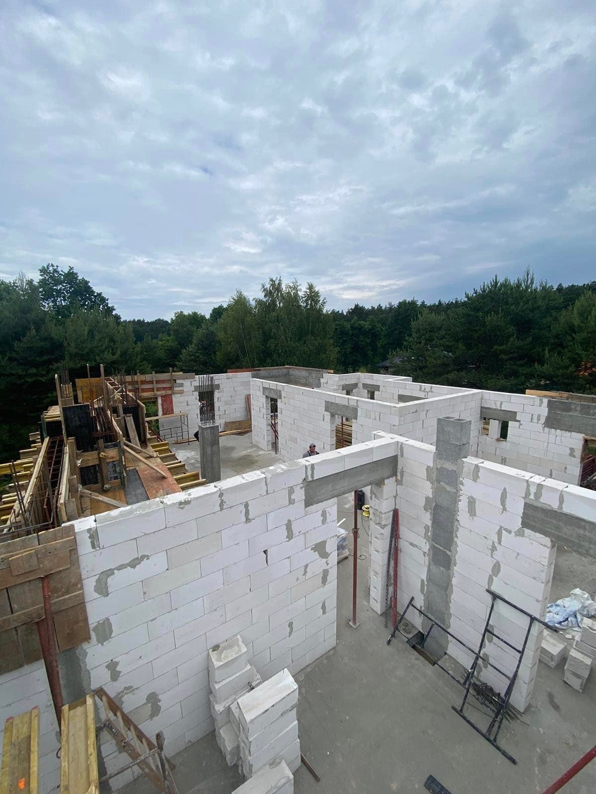 Budowa domu z bloczków betonu komórkowego Ytong: widok z góry na wznoszone ściany działowe i nośne, drewniane szalunki pod wylewki, betonowe nadproża, zbrojenia pionowe w słupach, drabina i paleta...