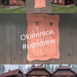 Dom z bali z drewnianymi, dekoracyjnymi okiennicami w kształcie serc, malowanymi na czerwono, otoczony zielenią.