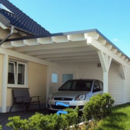 Pdn.drew - Biała, drewniana konstrukcja zadaszenia nad miejscem parkingowym, przylegająca do domu z szarym dachem, z zaparkowanym srebrnym samochodem osobowym.