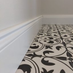 Pdn.drew - Czarno-biała, wzorzysta podłoga z płytek ceramicznych, przycięta białą listwą przypodłogową, widok z niskiej perspektywy.