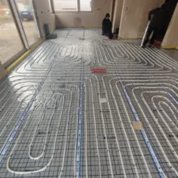 Instalacja ogrzewania podłogowego z rur Keller na siatce w surowym wnętrzu, widoczni dwaj instalatorzy w trakcie pracy.