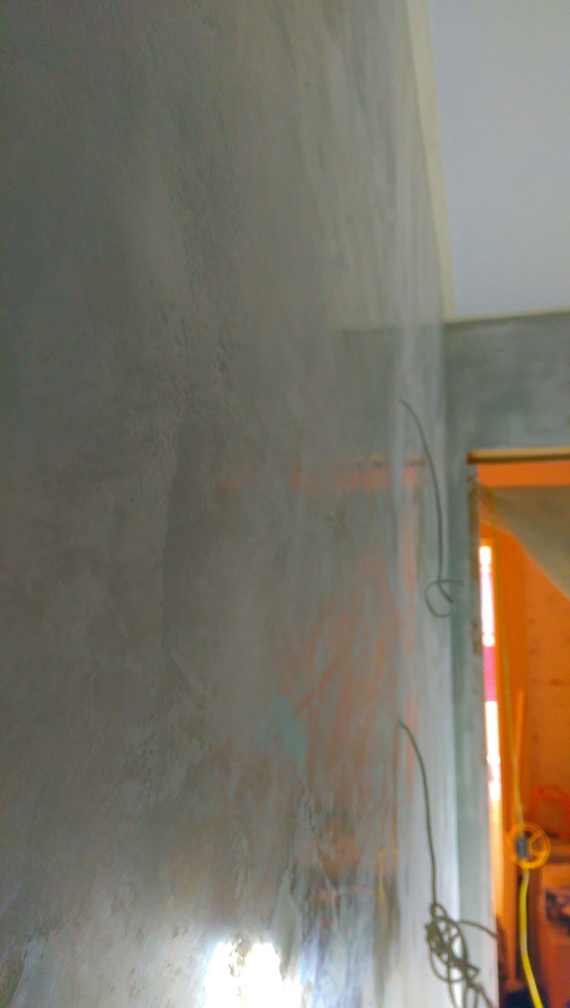 Ściana z efektem dekoracyjnym, szara z delikatnymi smugami, widoczne niedokończone prace elektryczne w tle.