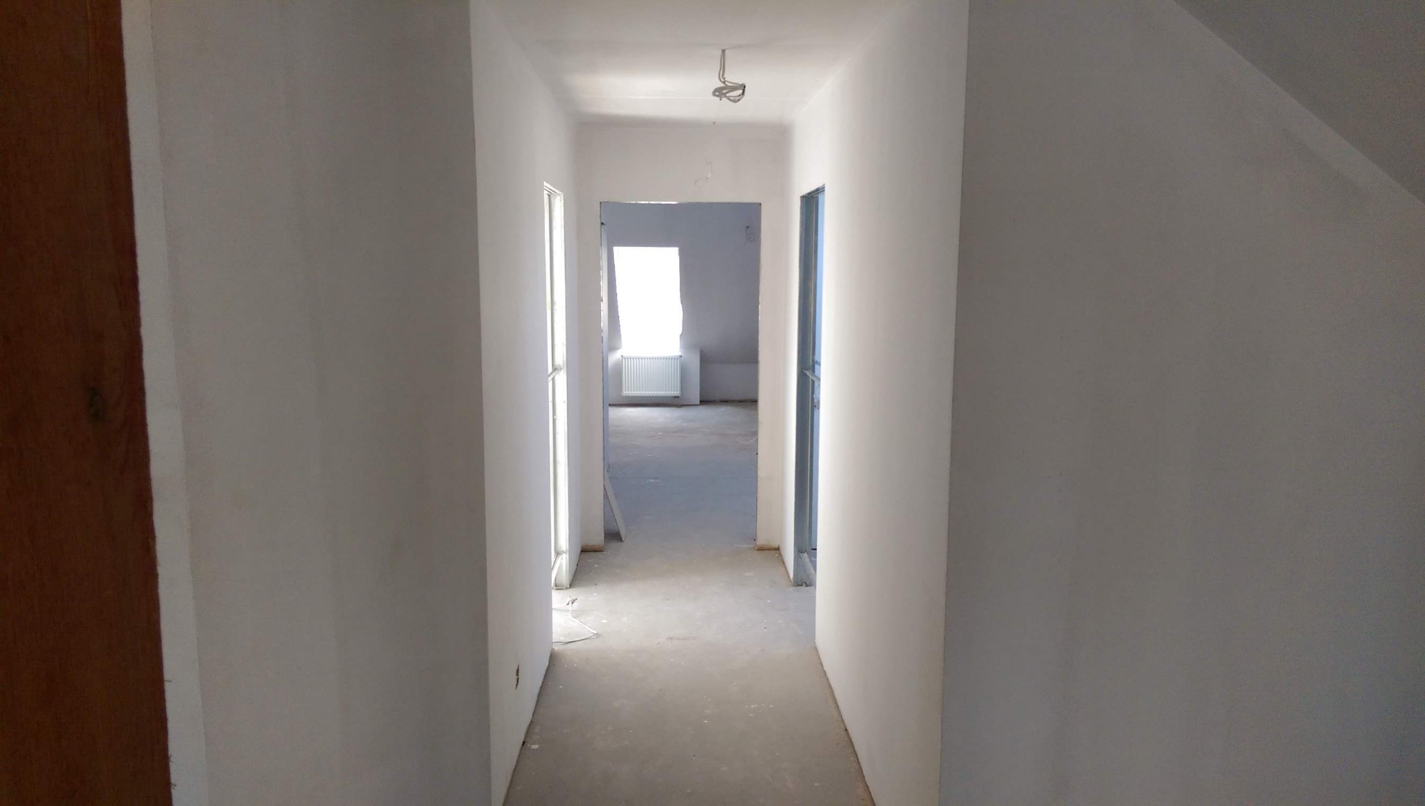 Korytarz w trakcie prac przygotowawczych do malowania, ściany pokryte gładzią, widoczne przewody oświetleniowe na suficie.