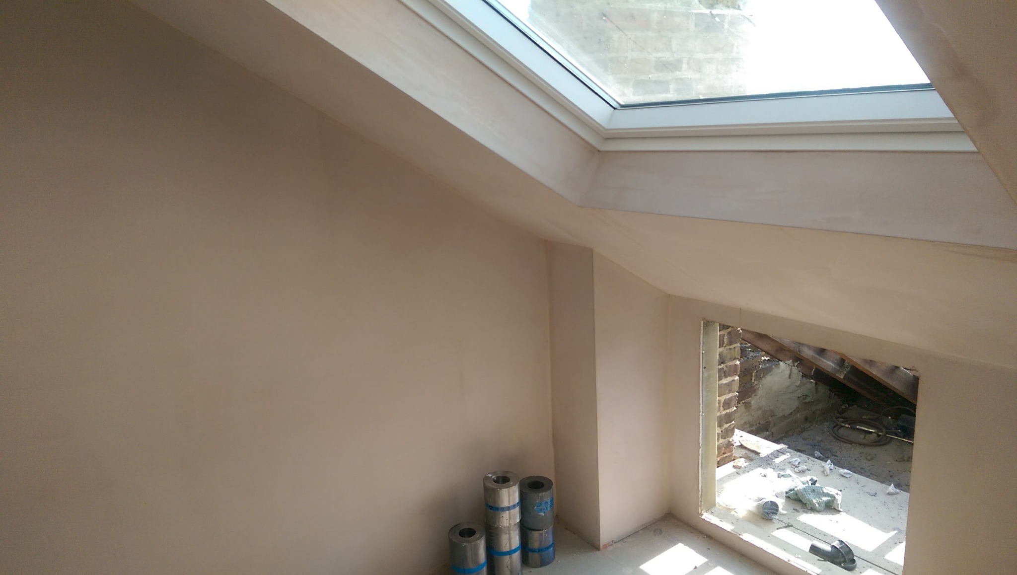 Poddasze po szpachlowaniu ścian i sufitu z oknem dachowym, widoczne rolki ołowiu pod ścianą.