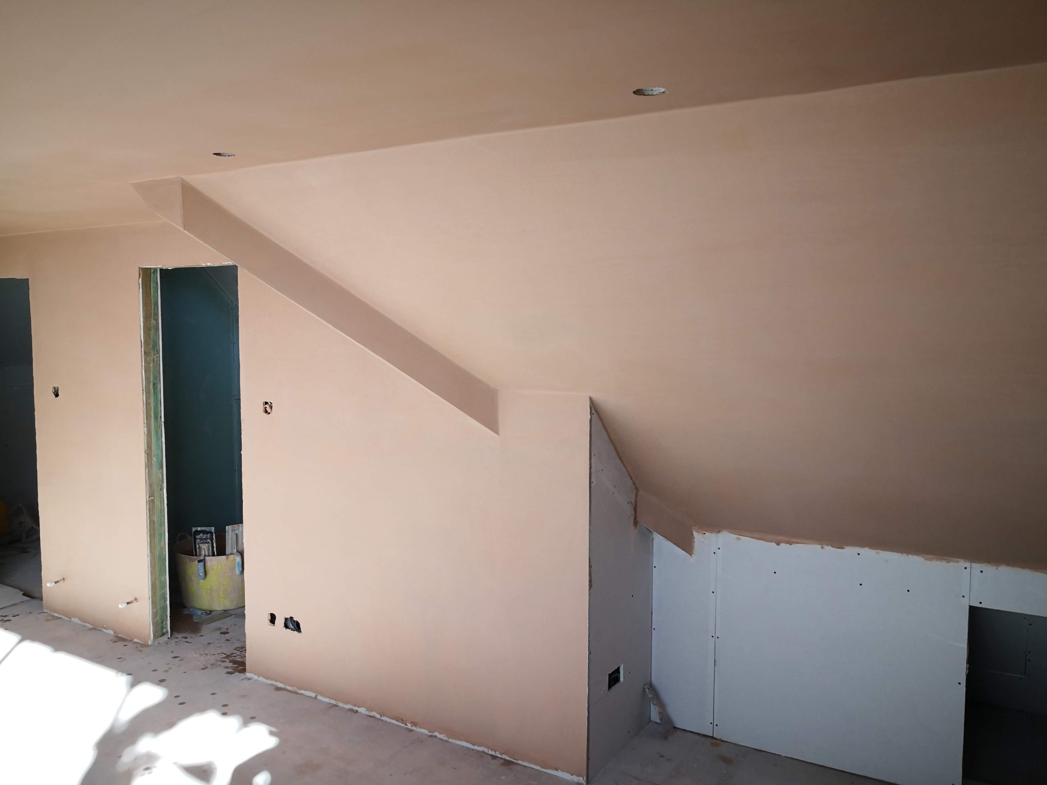 Skośny sufit i ściany po szpachlowaniu, widoczne otwory na gniazdka elektryczne, fragment ściany z płyt kartonowo-gipsowych, przygotowanie do malowania.