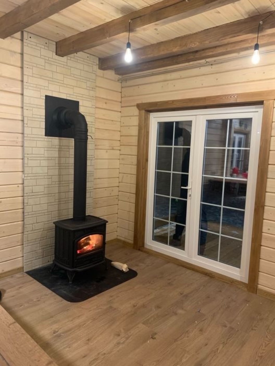 Czarny piec wolnostojący z płomieniami w drewnianym wnętrzu domu z boazerią i oknami.