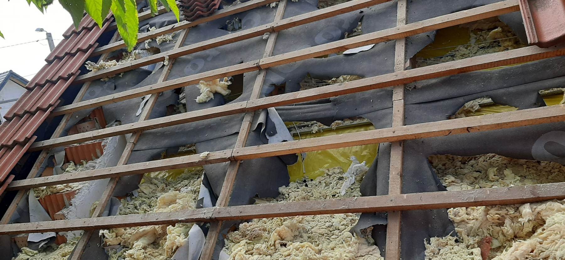 Fragment dachu w trakcie remontu, widoczne drewniane krokwie, uszkodzona membrana, izolacja z wełny mineralnej i fragment czerwonej dachówki