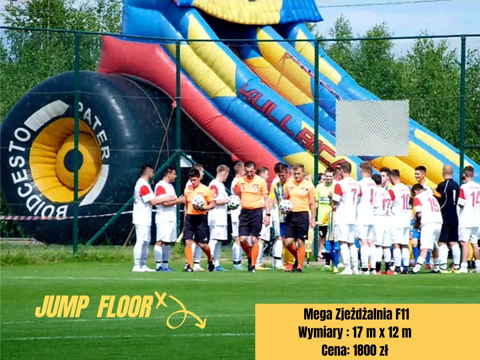 Duża, kolorowa dmuchana zjeżdżalnia z motywem opony samochodowej, ustawiona na boisku sportowym, obok stoi grupa osób w strojach sportowych.