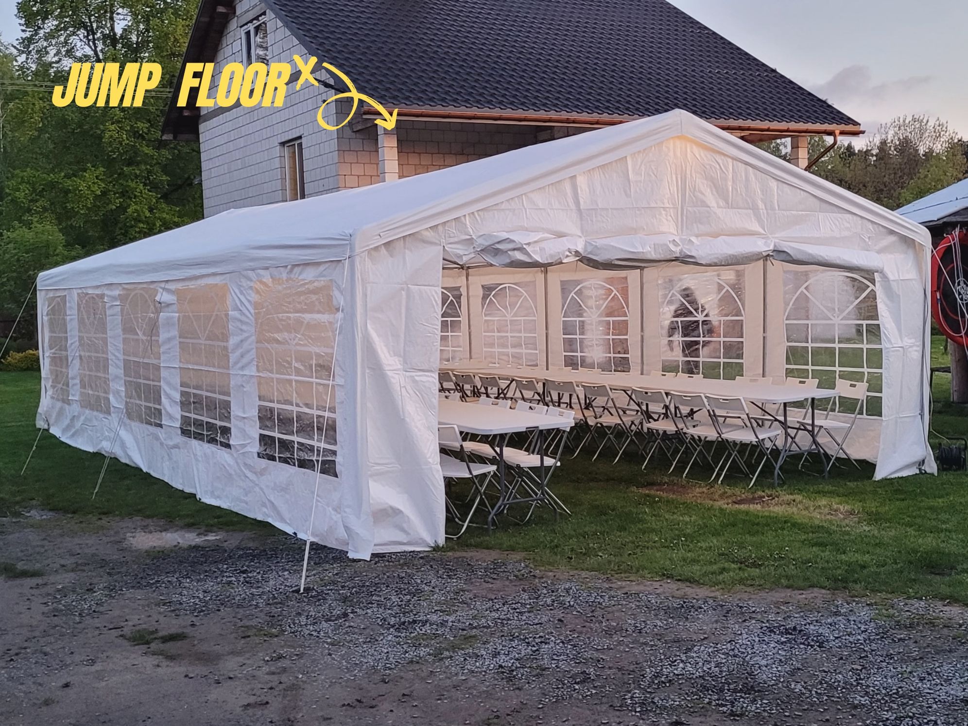 Biały namiot imprezowy rozstawiony na trawie obok domu, wewnątrz widoczne białe stoły i krzesła przygotowane na przyjęcie.