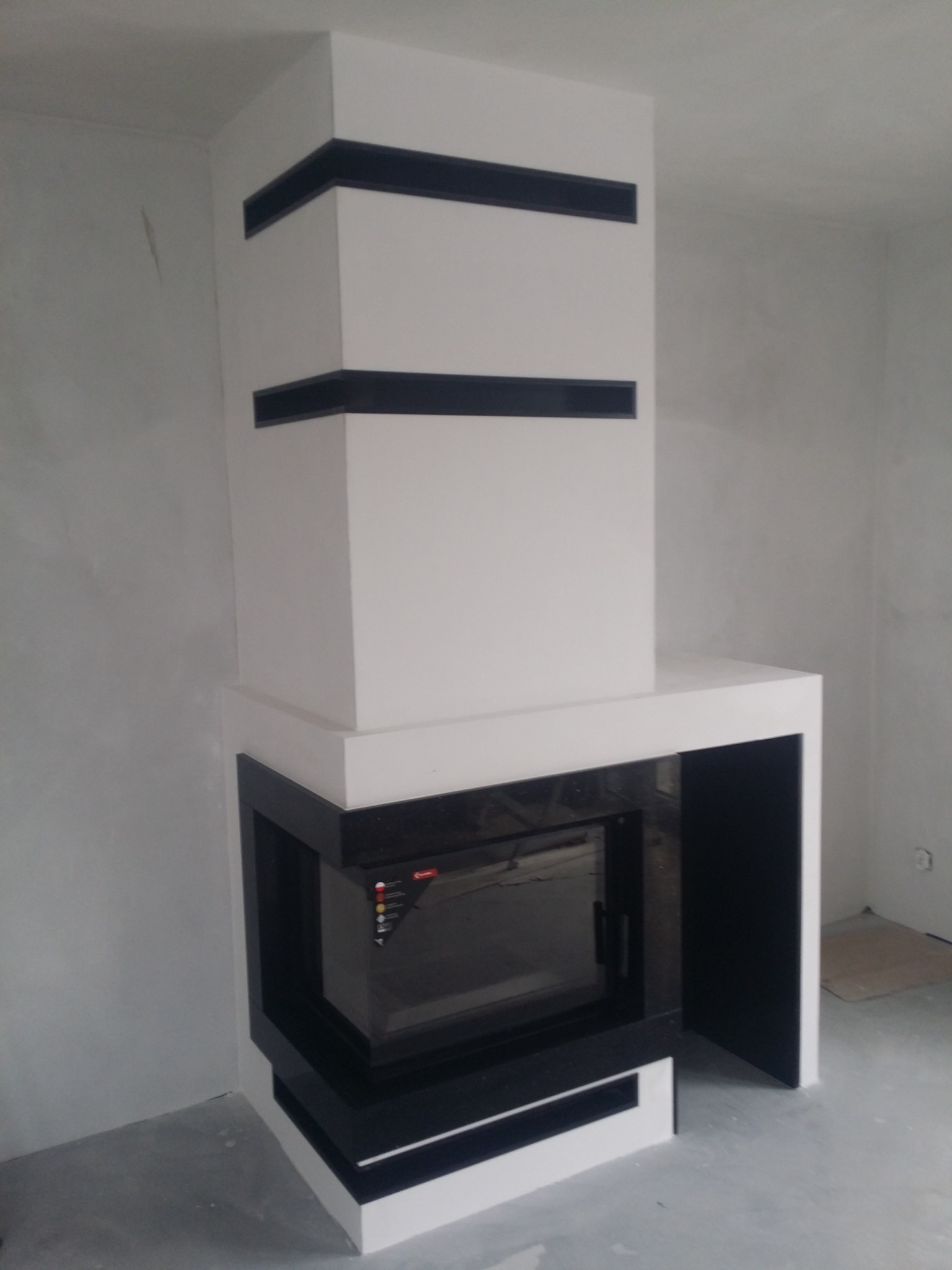 Nowoczesny obudowany wkład kominkowy z białymi i czarnymi elementami w surowym wnętrzu.