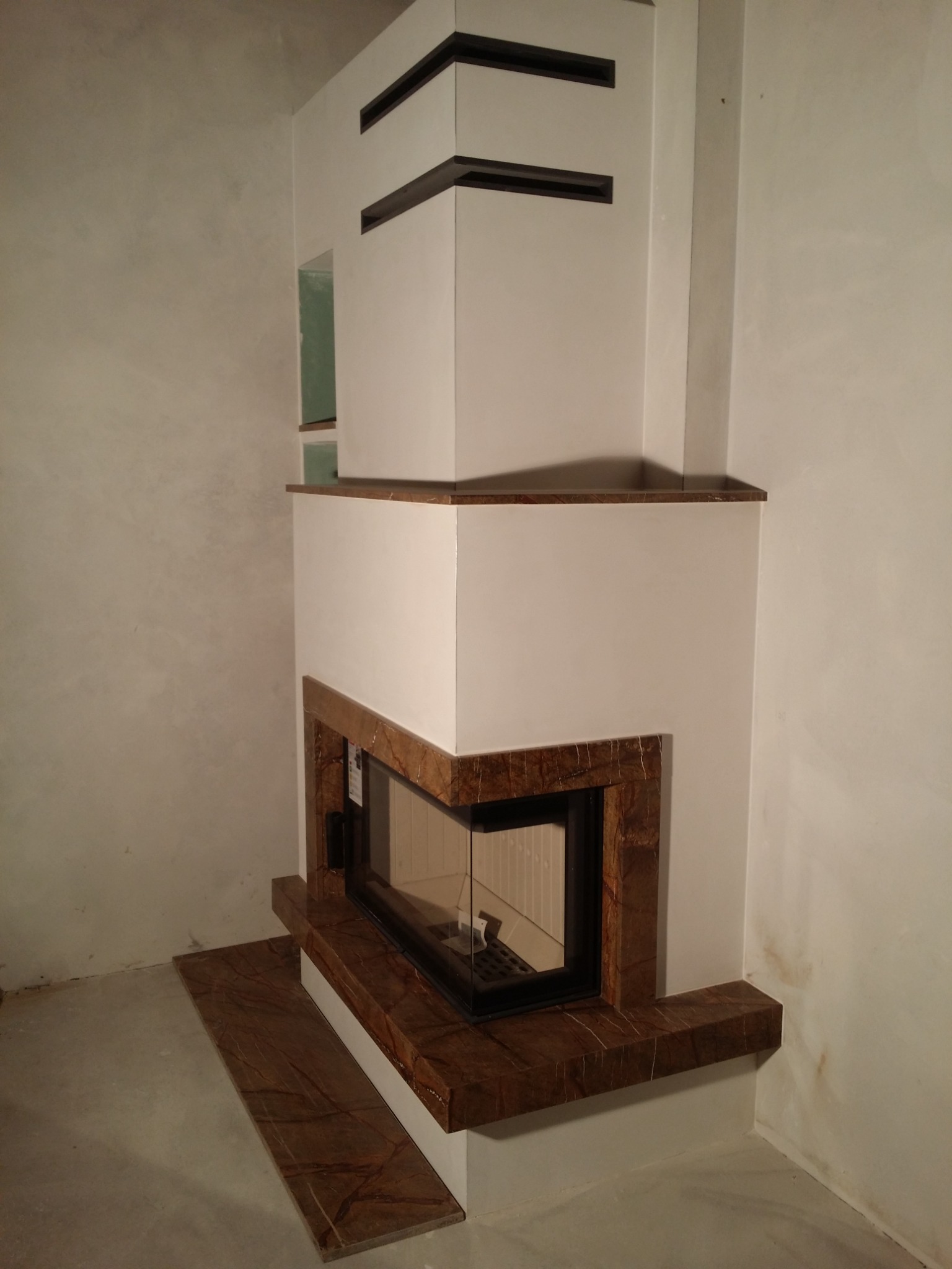 Nowoczesna obudowa wkładu kominkowego z marmurowym wykończeniem, widok z boku, surowy stan wykończenia ścian.