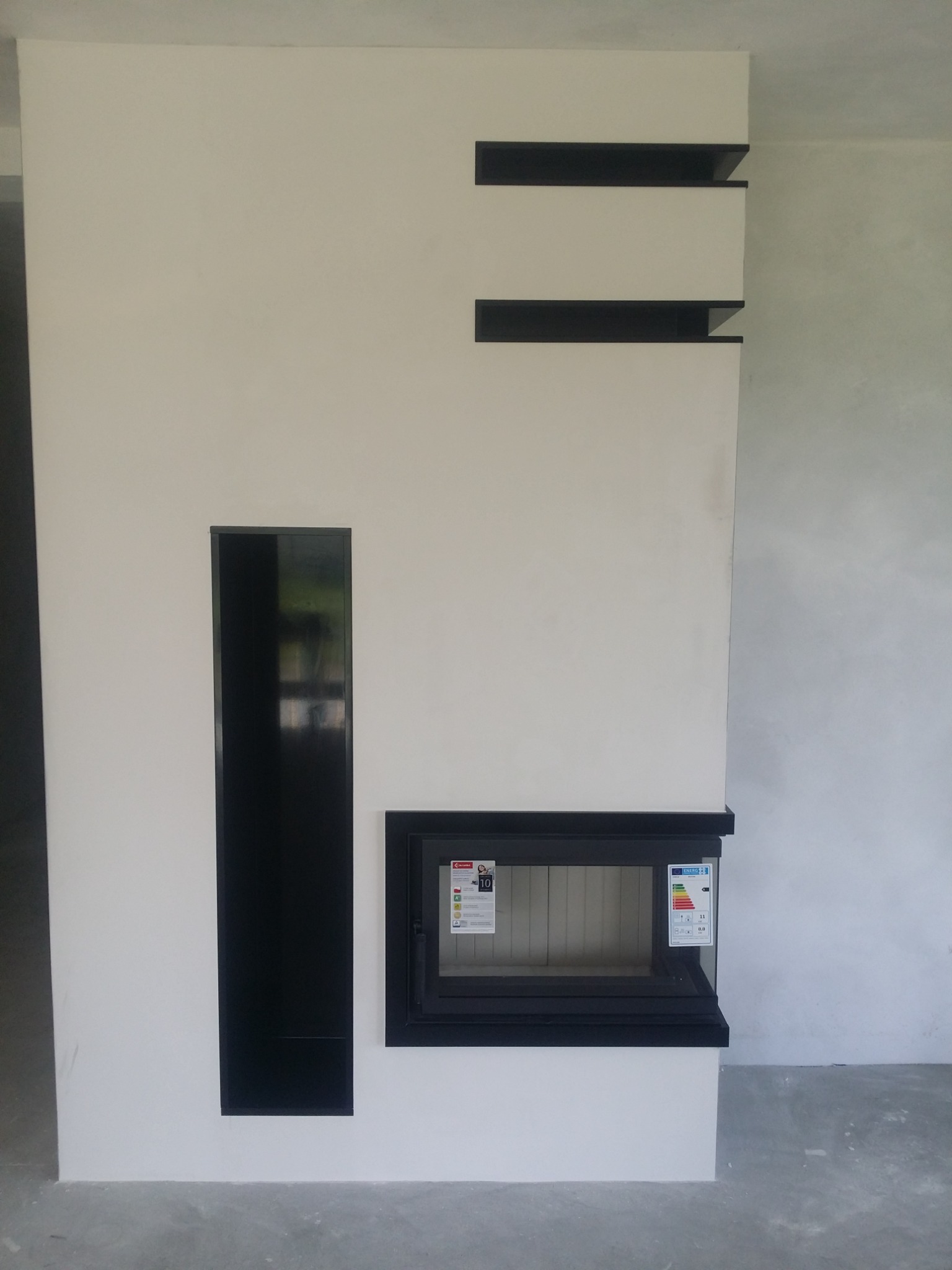 Nowoczesna obudowa kominkowa w Sieniawie, z czarnymi elementami dekoracyjnymi i wnęką, widoczne naklejki informacyjne na szybie.