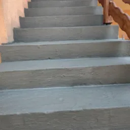 Wykończone betonowe schody zewnętrzne z drewnianą balustradą o falistym wzorze, pomalowane na szaro, widoczne z dołu.