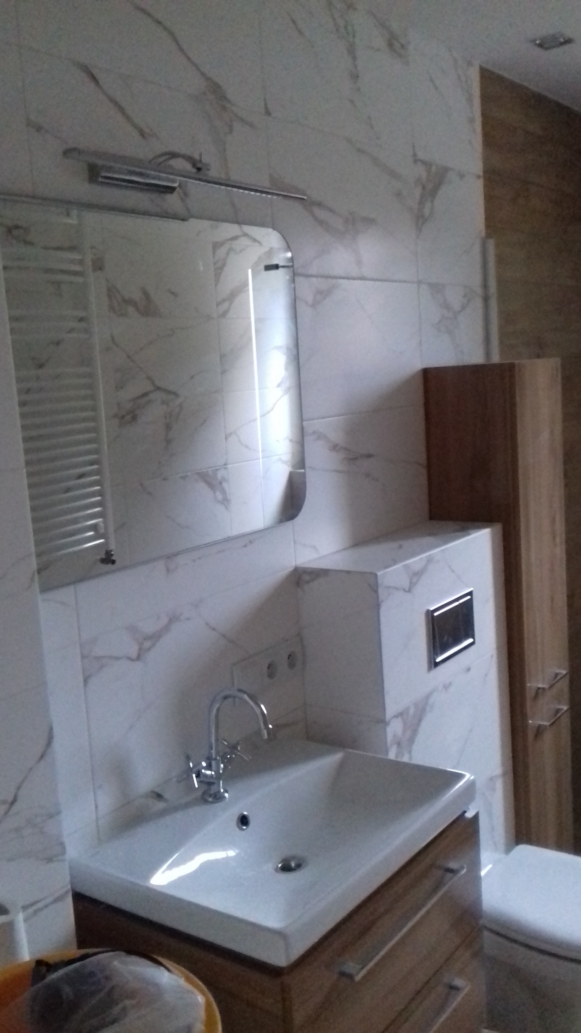 Nowoczesna łazienka z umywalką nablatową na drewnianej szafce, marmurowe płytki na ścianach i lustro z oświetleniem LED.