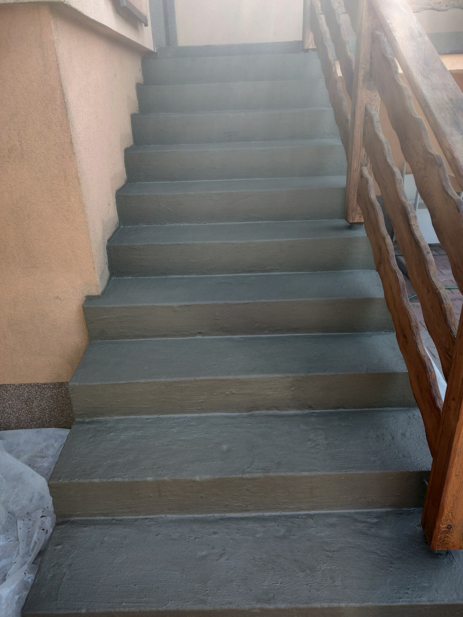 Schody betonowe po renowacji z drewnianą balustradą po prawej stronie, widoczne ślady po malowaniu na folii ochronnej przy ścianie.