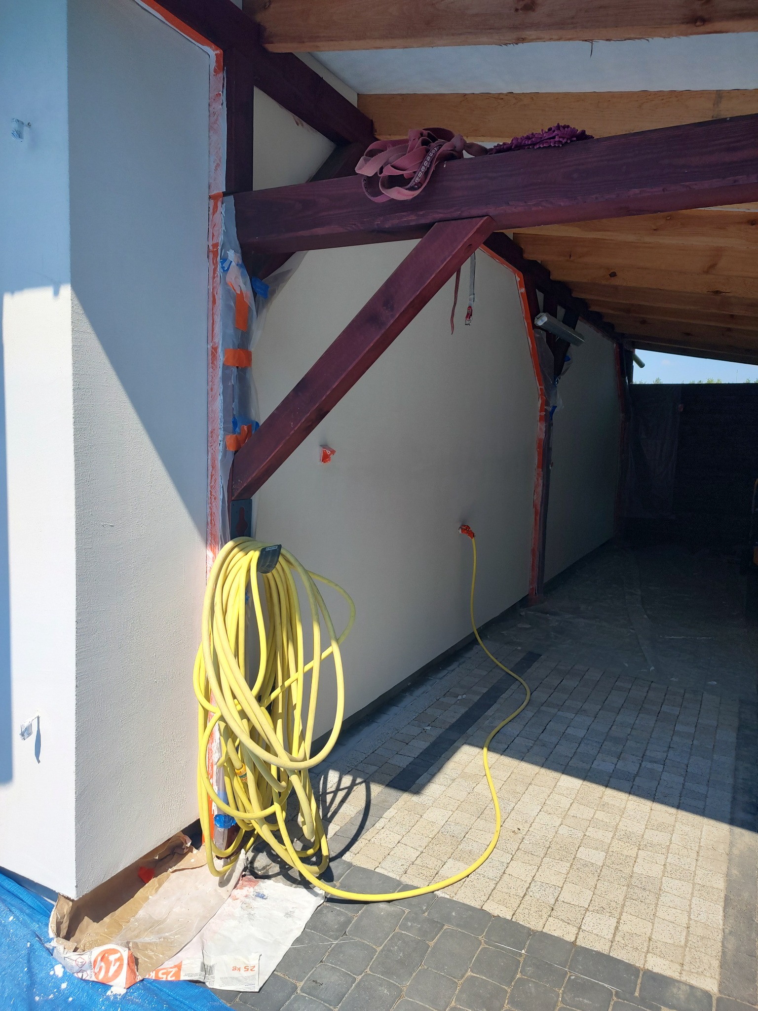 Ocieplona ściana zewnętrzna domu w trakcie prac wykończeniowych, z widoczną żółtą rurą i zabezpieczeniami okiennymi, przygotowana do nałożenia gładzi.