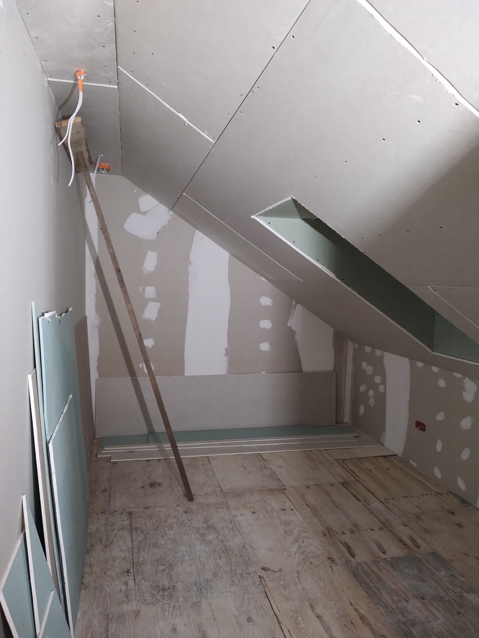 Poddasze w trakcie wykańczania płytami gipsowo-kartonowymi; widoczne szpachlowane łączenia, odsłonięta instalacja elektryczna i stos płyt przy ścianie.