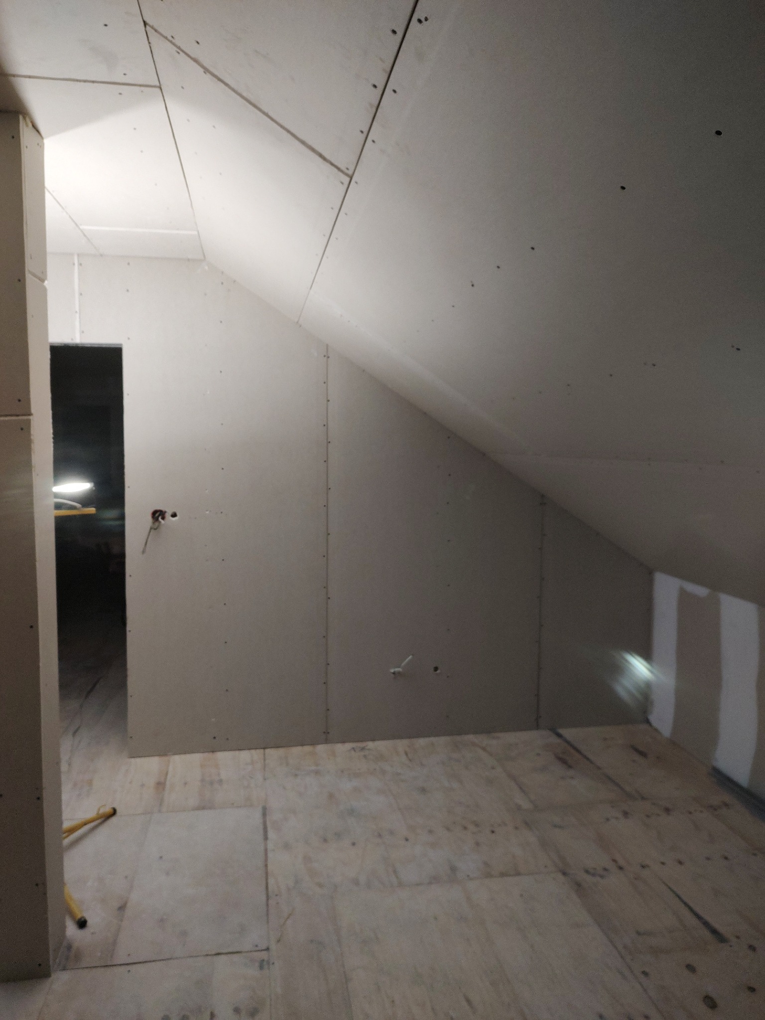 Poddasze w trakcie wykańczania płytami kartonowo-gipsowymi, widoczne łączenia i wkręty, surowa podłoga z płyt OSB, wystające przewody elektryczne.